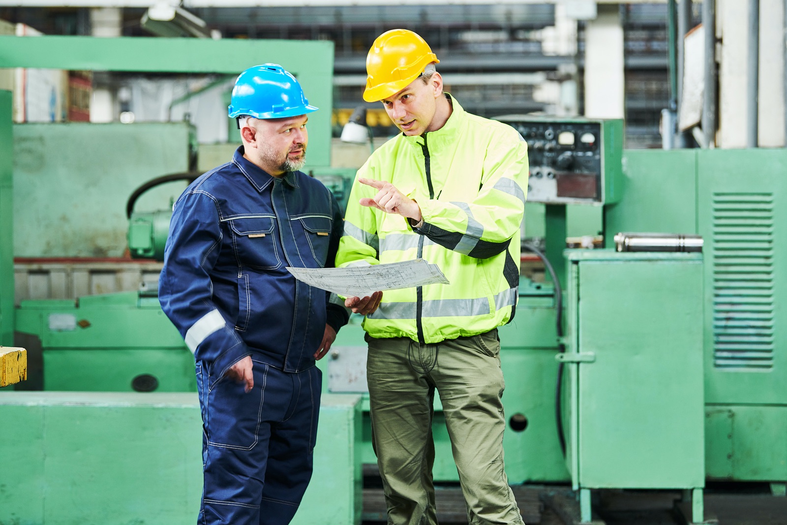 Two men in hard hats and safety jackets talking.